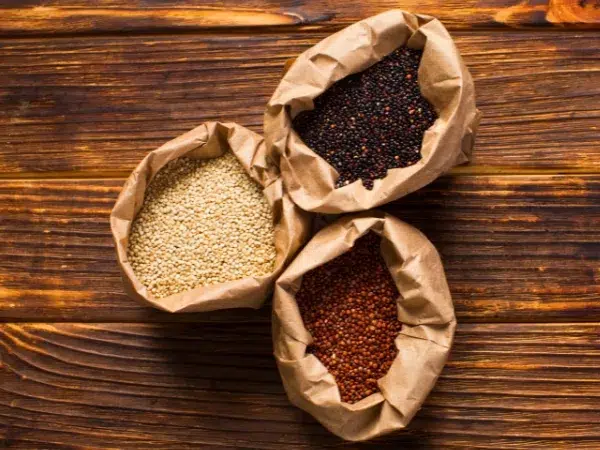 3 variétés de quinoa dans des sachets: blanc, noir et rouge sous fond de bois.