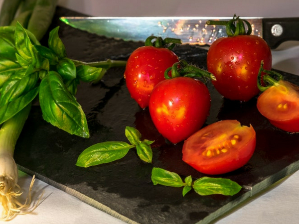 planche à découper avec tomates et feuilles de basilic avecun couteau