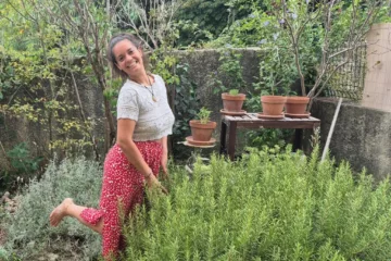 Caroline dans son jardin avec une jupe rouge un haut blanc et un romarin