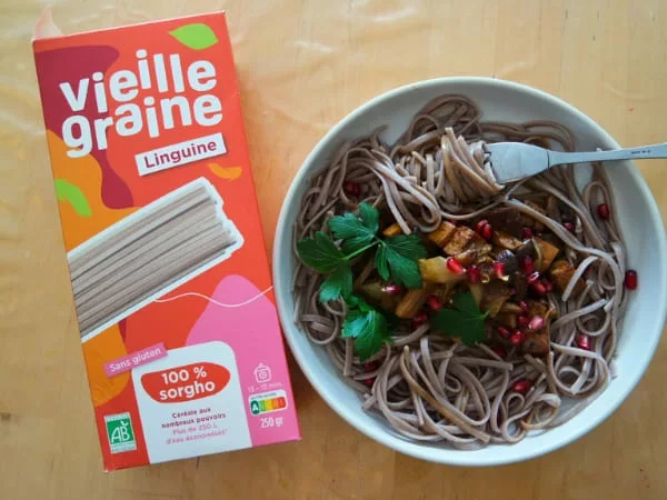 Paquet de pâtes avec une assiette de pâtes des légumes, du persil et une fourchette.