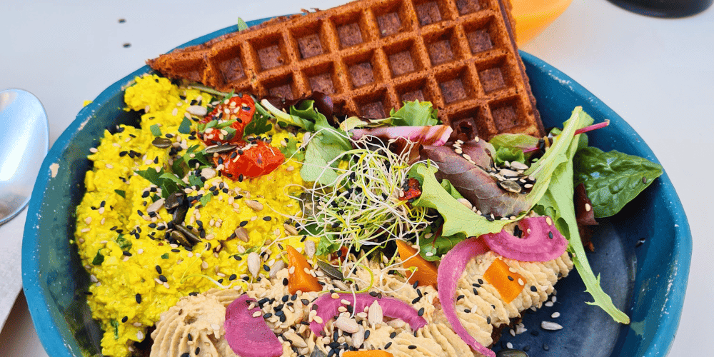Assiette végétale colorée avec une gaufre du houmous et de la salade