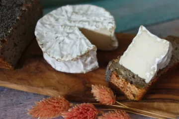 Fromage vegan comme du camembert coupé sur une planche en bois avec des fleurs séchées