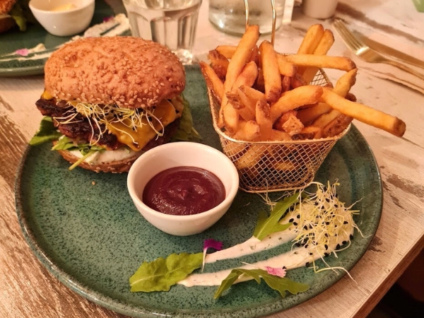 Assiette de burger vegan et sans gluten avec des frites maison, sauce ketchup et graines germées sur une assiette verte