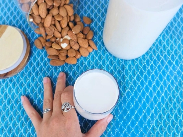 Lait d'amande dans un verre et une bouteille en verre. Amandes crues sur une nappe bleue