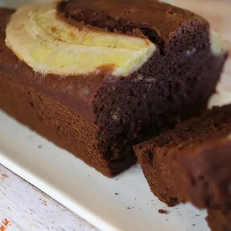 Gâteau chocolat banane moelleux avec une demi banane dessus sur une assiette blanche