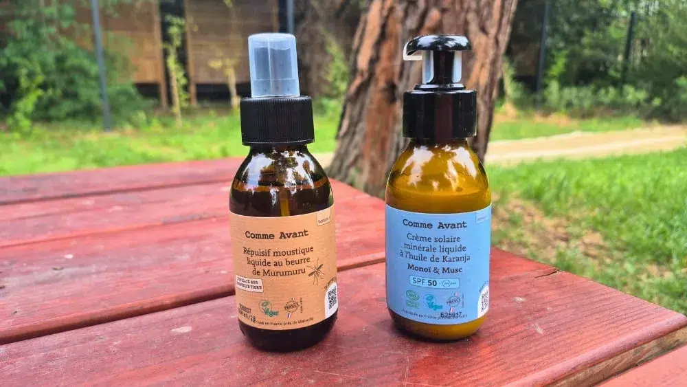 Répulsif anti-moustique liquide au beurre de murumuru et Crème solaire SPF50 minérale liquide à l'huile de karanja marque Comme Avant présentés sur une table avec un tronc d'arbre derrière