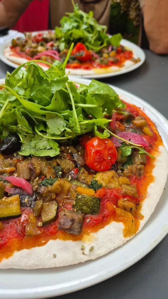 Pizza sans gluten et vegan avec salade roquette, olives noires et tomates cerises